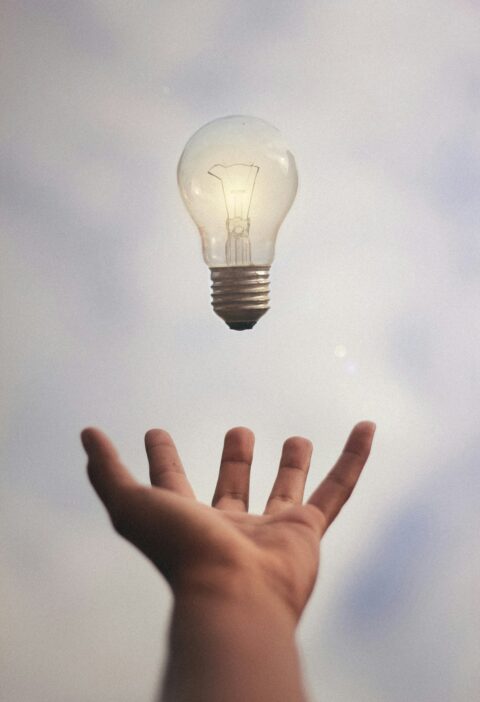 Schwebende Glübirne oberhalb einer ausgestreckten Hand.